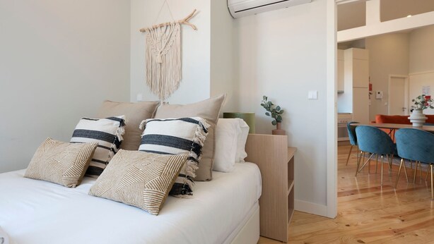 Une chambre moderne avec un lit, une décoration murale en macramé et une vue sur l’espace salle à manger.
