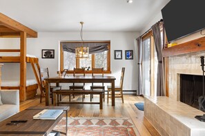 A cozy living room with a wooden dining table, benches, and a fireplace.