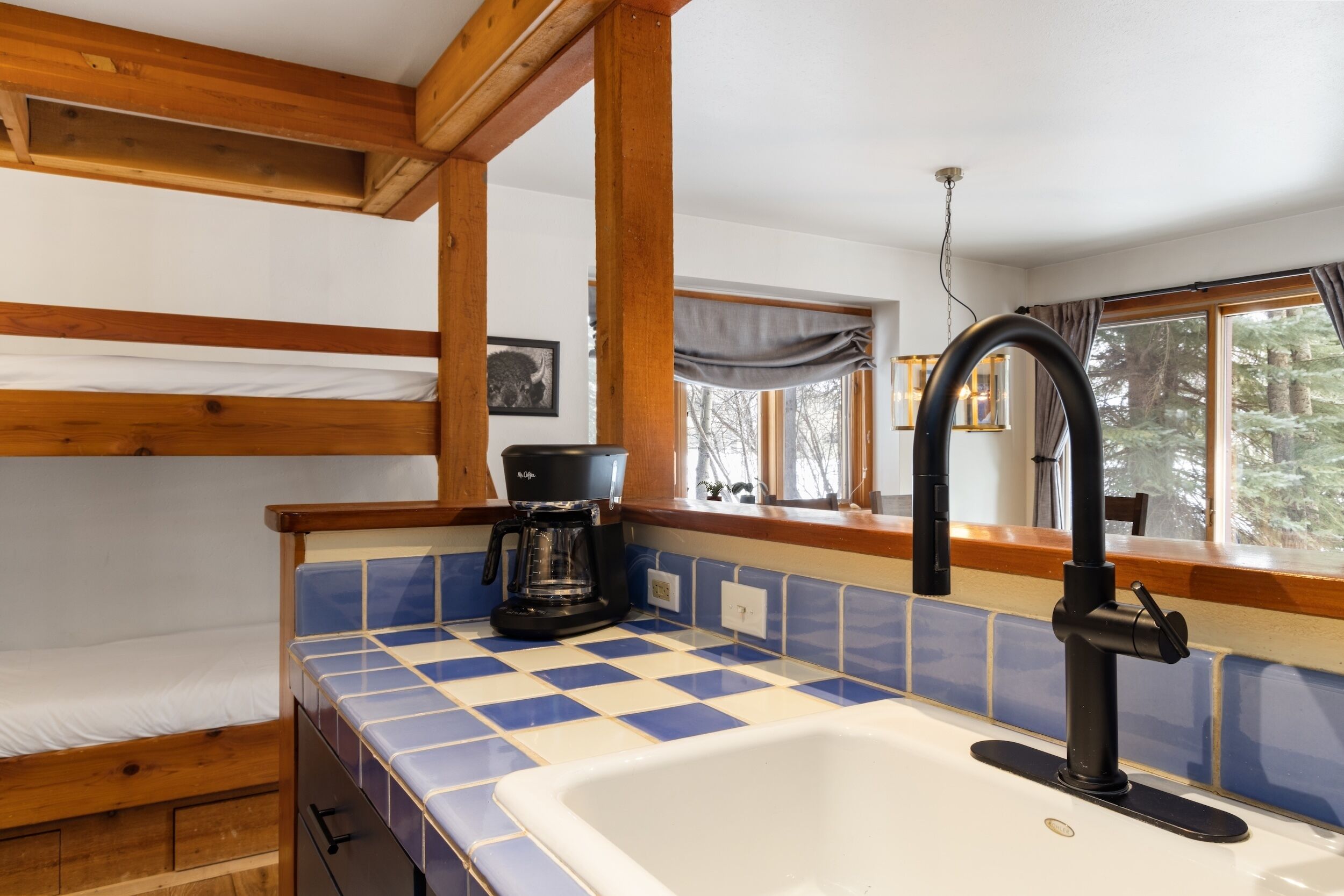 A kitchen with a checkered blue and white tile backsplash, a white sink, and a coffee maker.