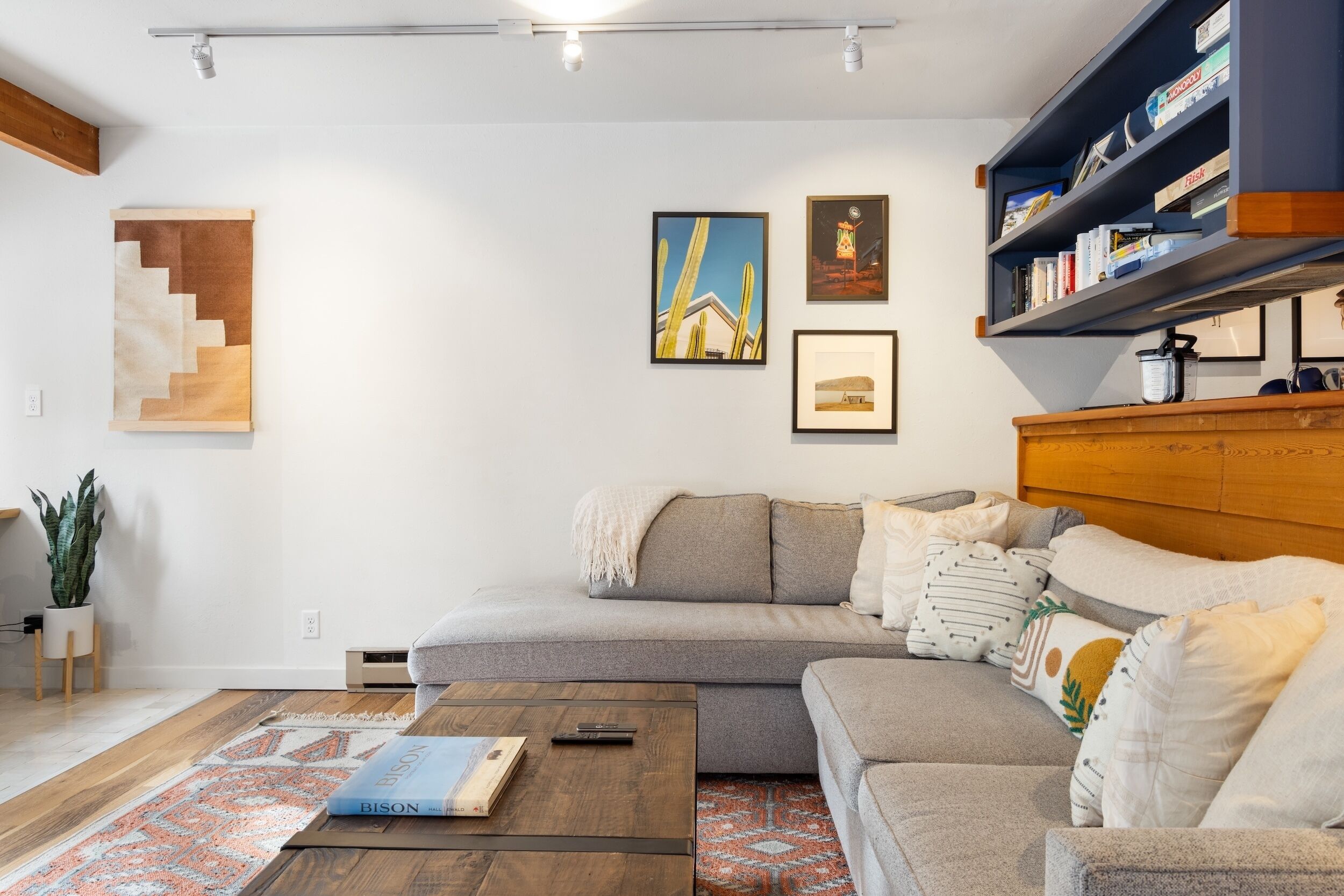 A modern living room with a grey sectional sofa, a wooden coffee table, and a bookshelf.