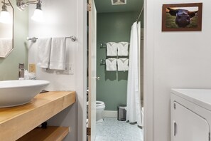 A bathroom with a large white sink, a mirror, and a wooden countertop. There are white towels hanging on a rack, and a picture of a cow on the wall.