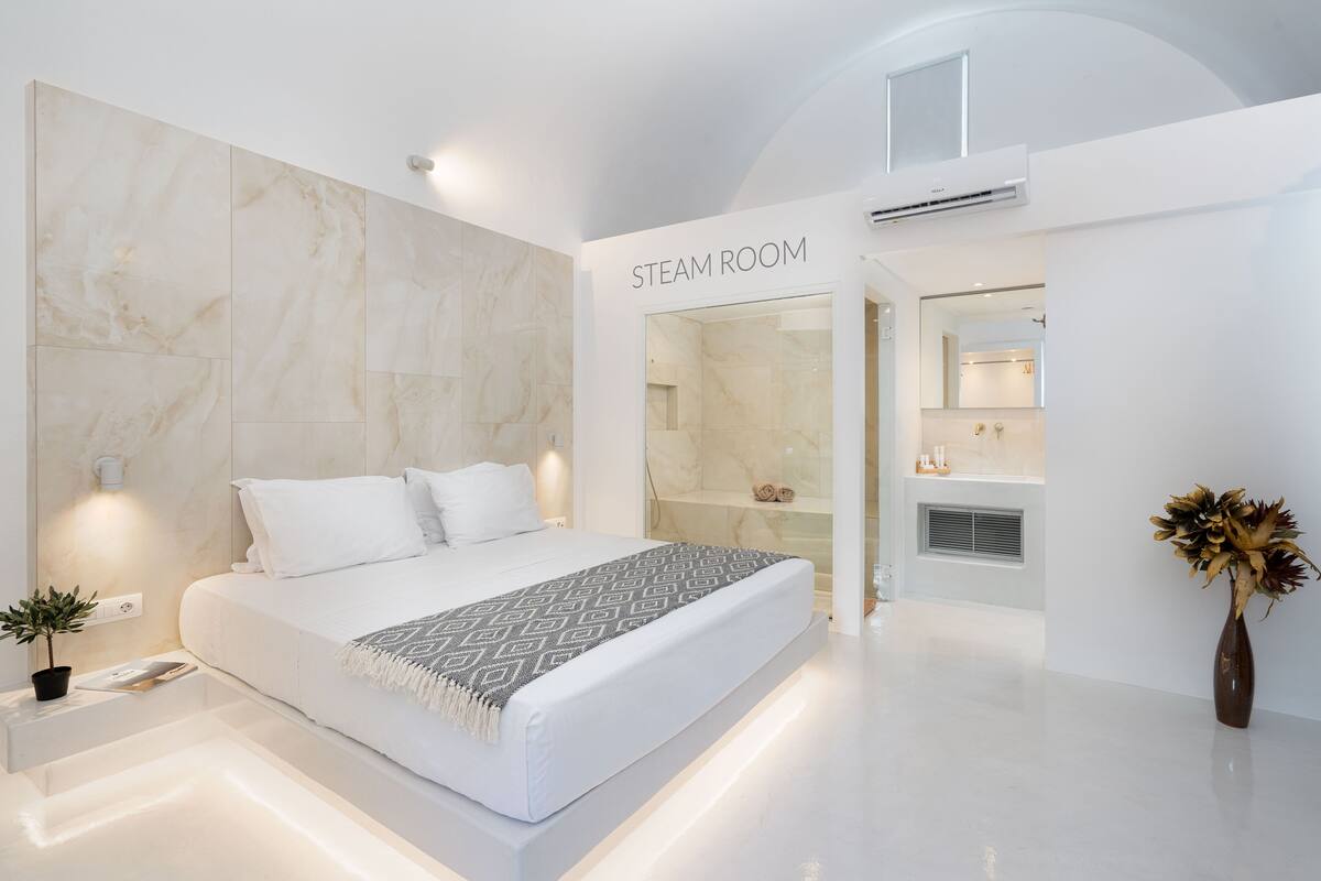 A modern hotel room with a large bed, a steam room, and a bathroom with a mirror and sink.