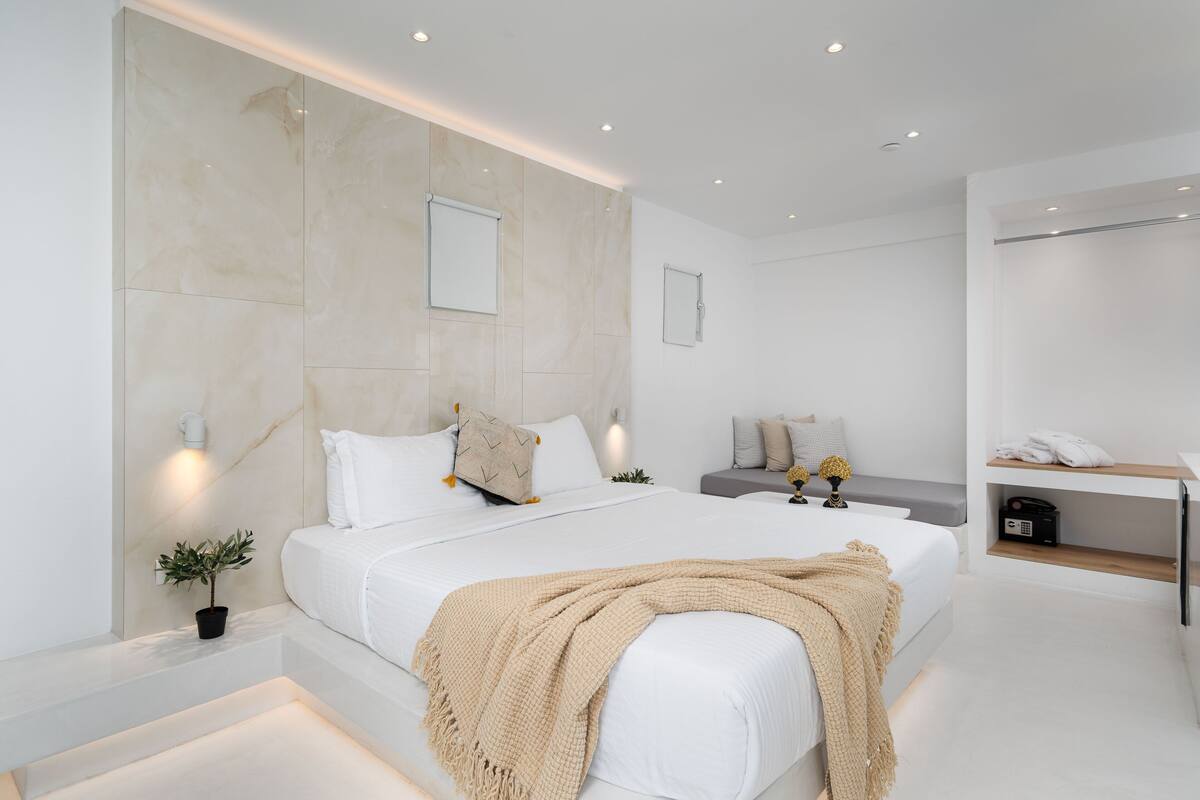 A modern bedroom with a large bed, bedside tables, a small seating area, and a built-in shelf with a radio.