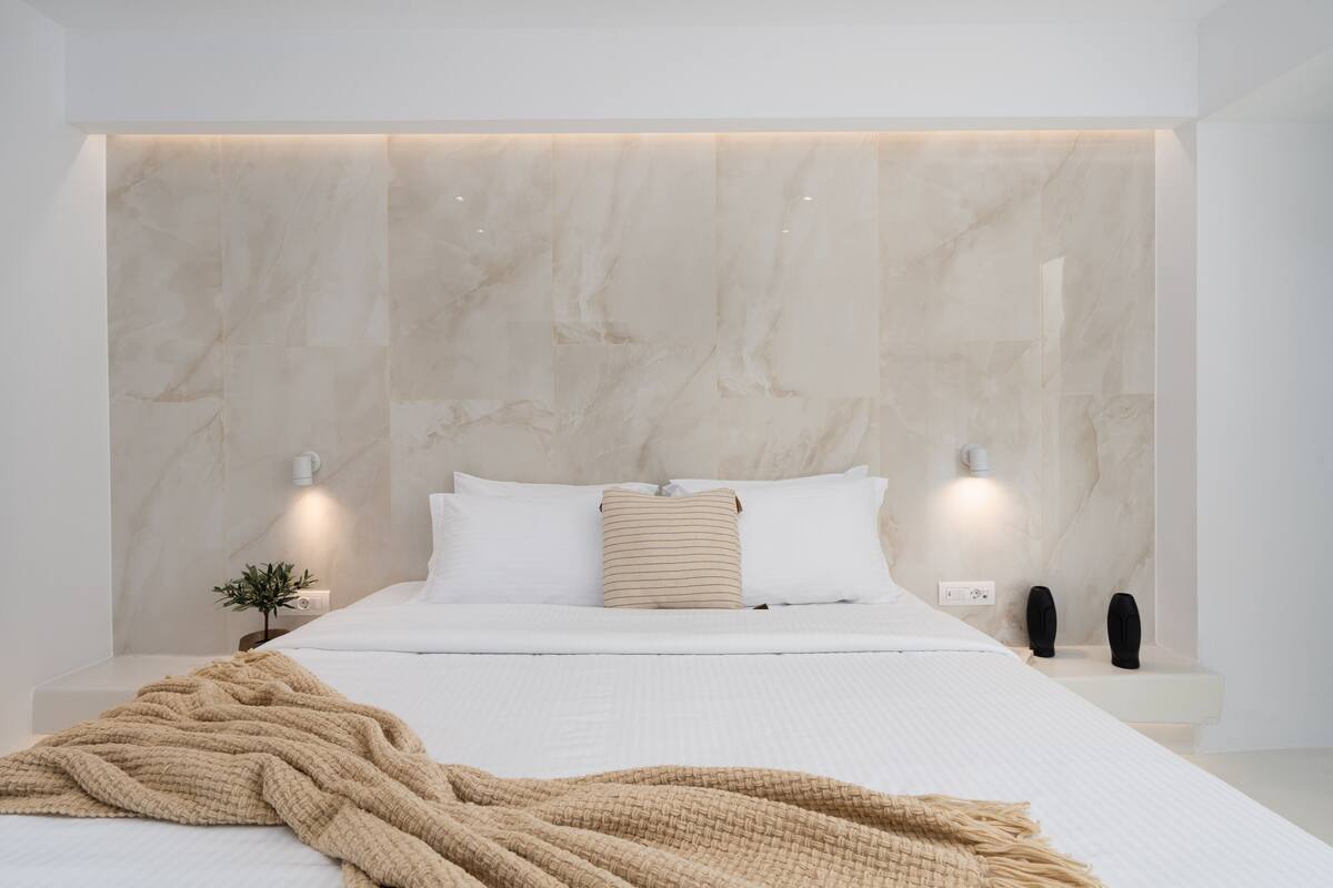 A modern bedroom with a large bed, a marble headboard, bedside lamps, and a small plant.