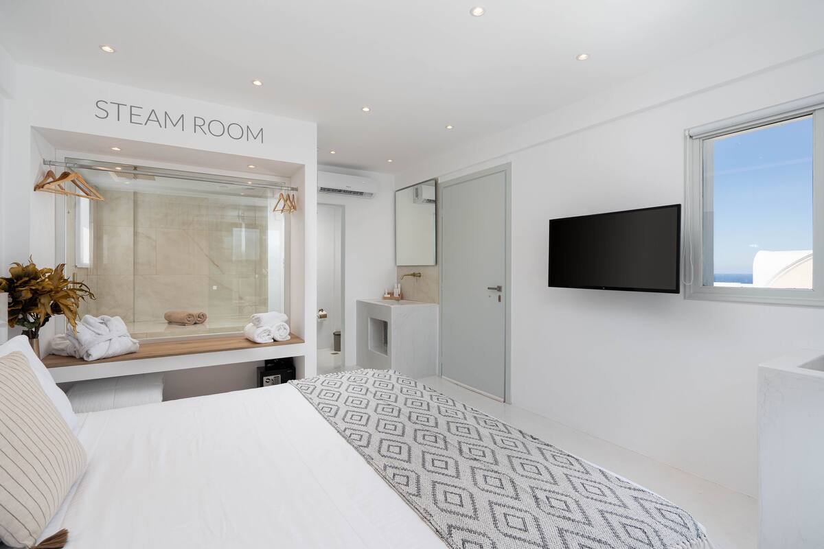 A modern steam room with a large mirror, a flat-screen TV, and a view of the sea.
