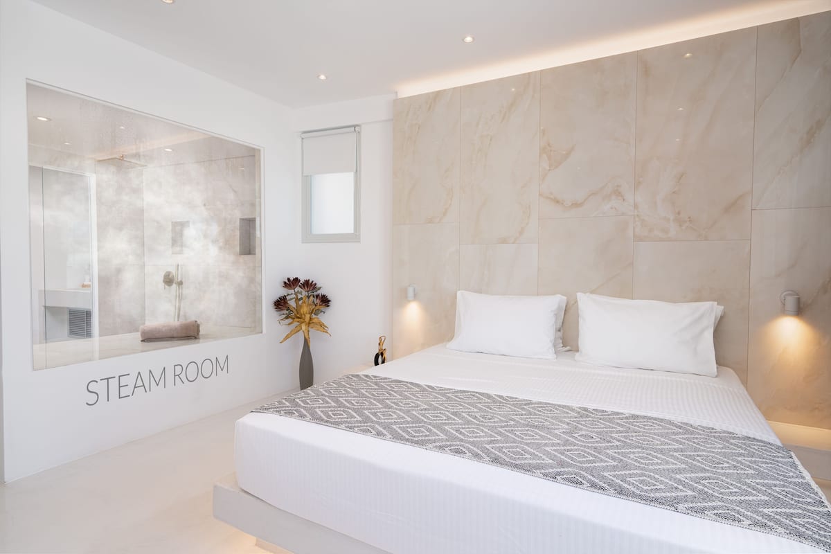 A modern steam room with a large mirror, a bed with white bedding, and a marble wall.