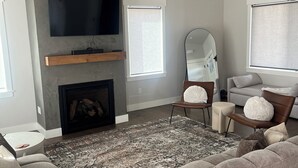 A modern living room with a large sectional sofa, a fireplace, a mounted TV, and a ceiling fan. - Beautiful brand new build with stunning mountain views (Missoula)