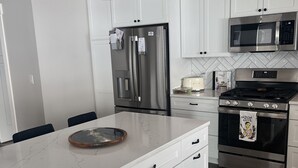 A modern kitchen with white cabinetry, stainless steel appliances, and a marble countertop. - Beautiful brand new build with stunning mountain views (Missoula)