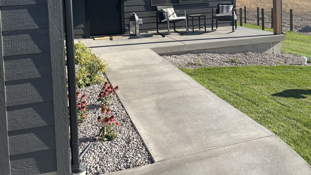 A modern house with a dark exterior, a covered porch with outdoor seating, and a clear view of the surrounding landscape. - Beautiful brand new build with stunning mountain views (Missoula)