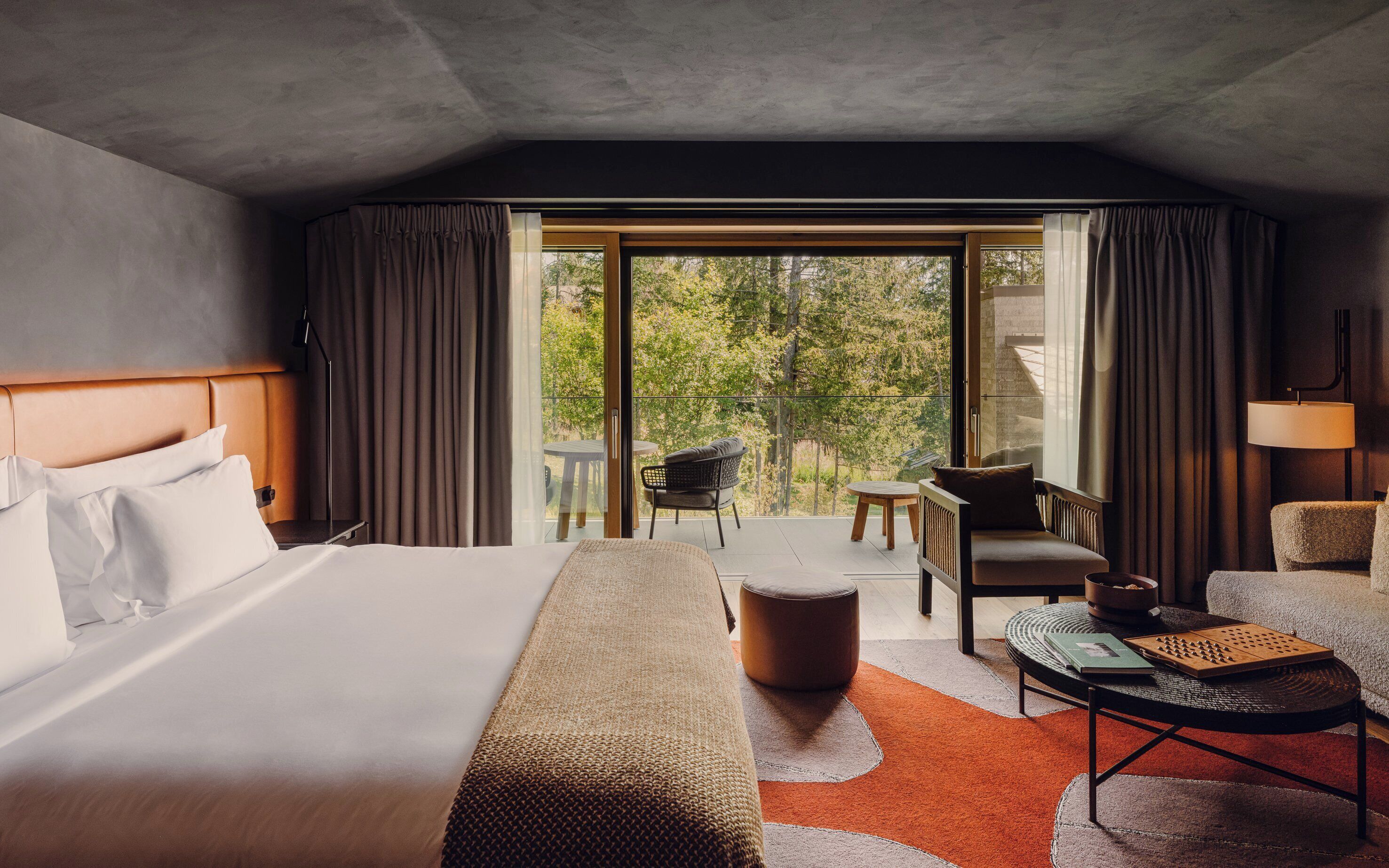 A hotel room with a large bed, a sofa, a dining table, and a view of the outdoors.