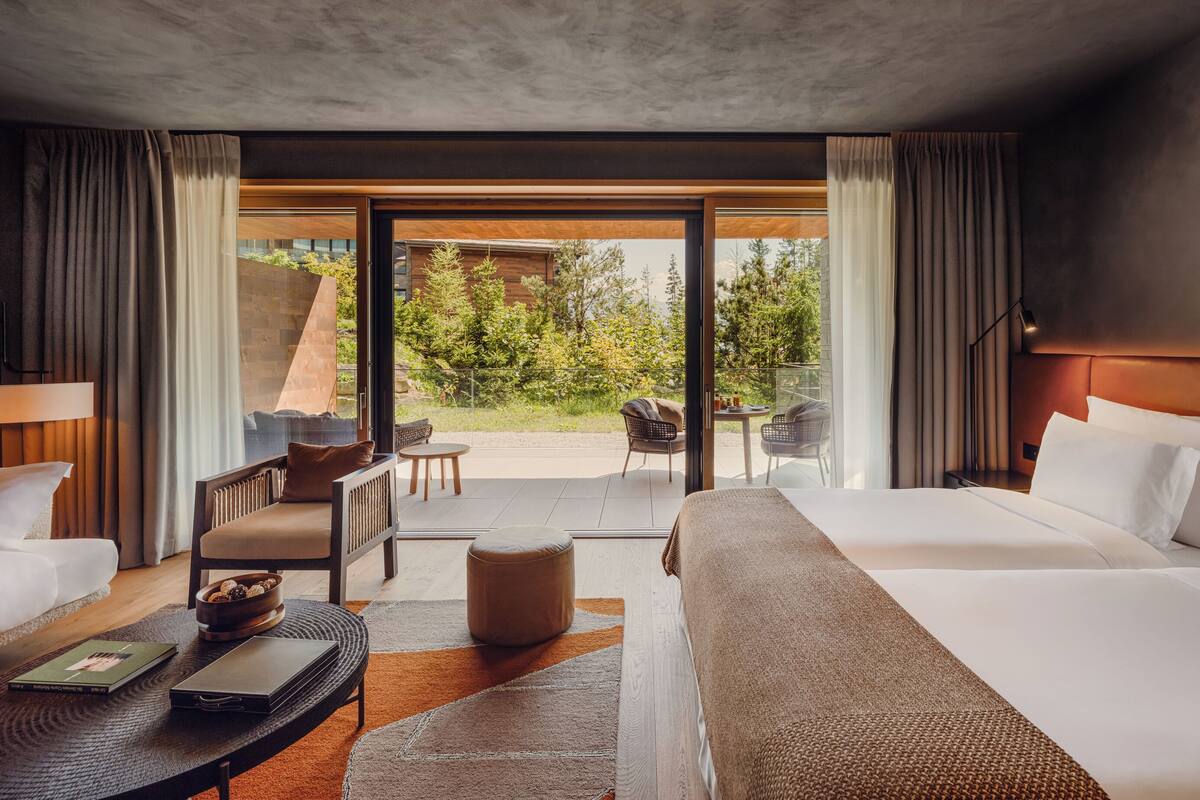 A modern hotel room with a large bed, a sofa, a small table, and a view of the outdoors.