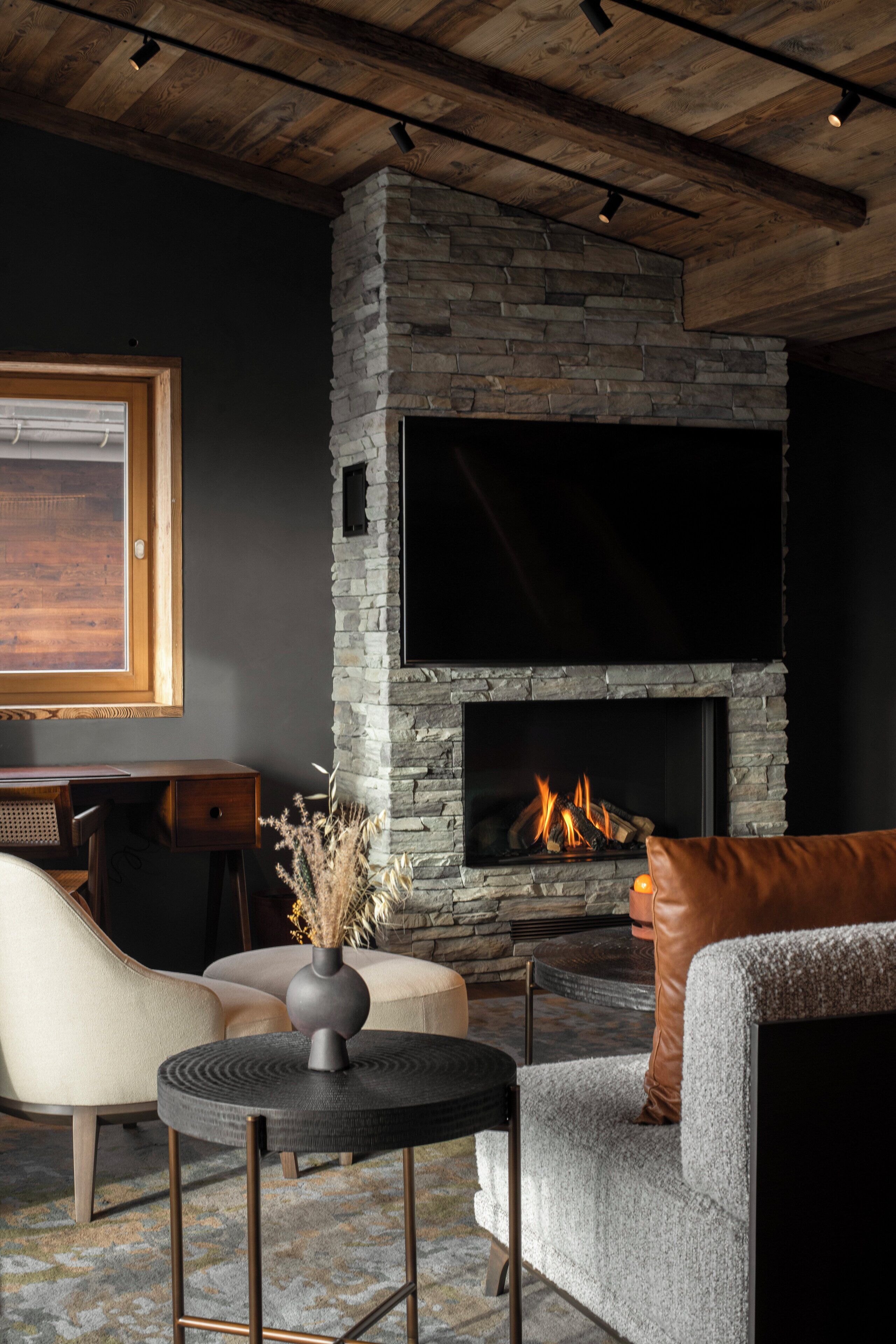 A modern living room with a stone fireplace, a comfortable sofa, a round coffee table, and a TV mounted above the fireplace.