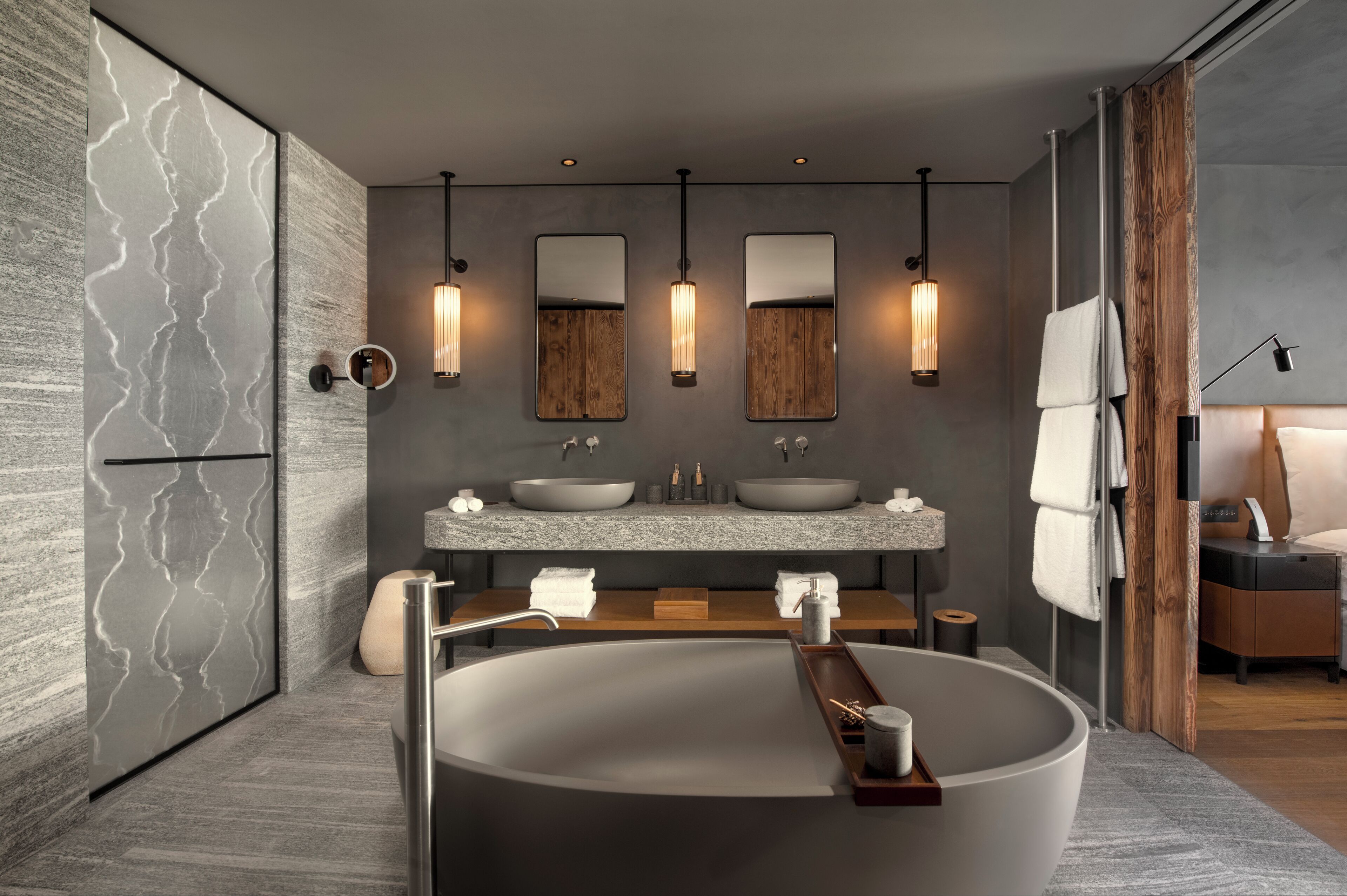 Un baño moderno con una bañera independiente grande, dos lavamanos con espejos e iluminación colgante.