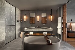 Un baño moderno con una bañera independiente grande, dos lavamanos con espejos e iluminación colgante.