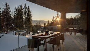 A dining area with a table set for two, overlooking a snowy landscape with trees and mountains. - Six Senses Crans-Montana (Lens)