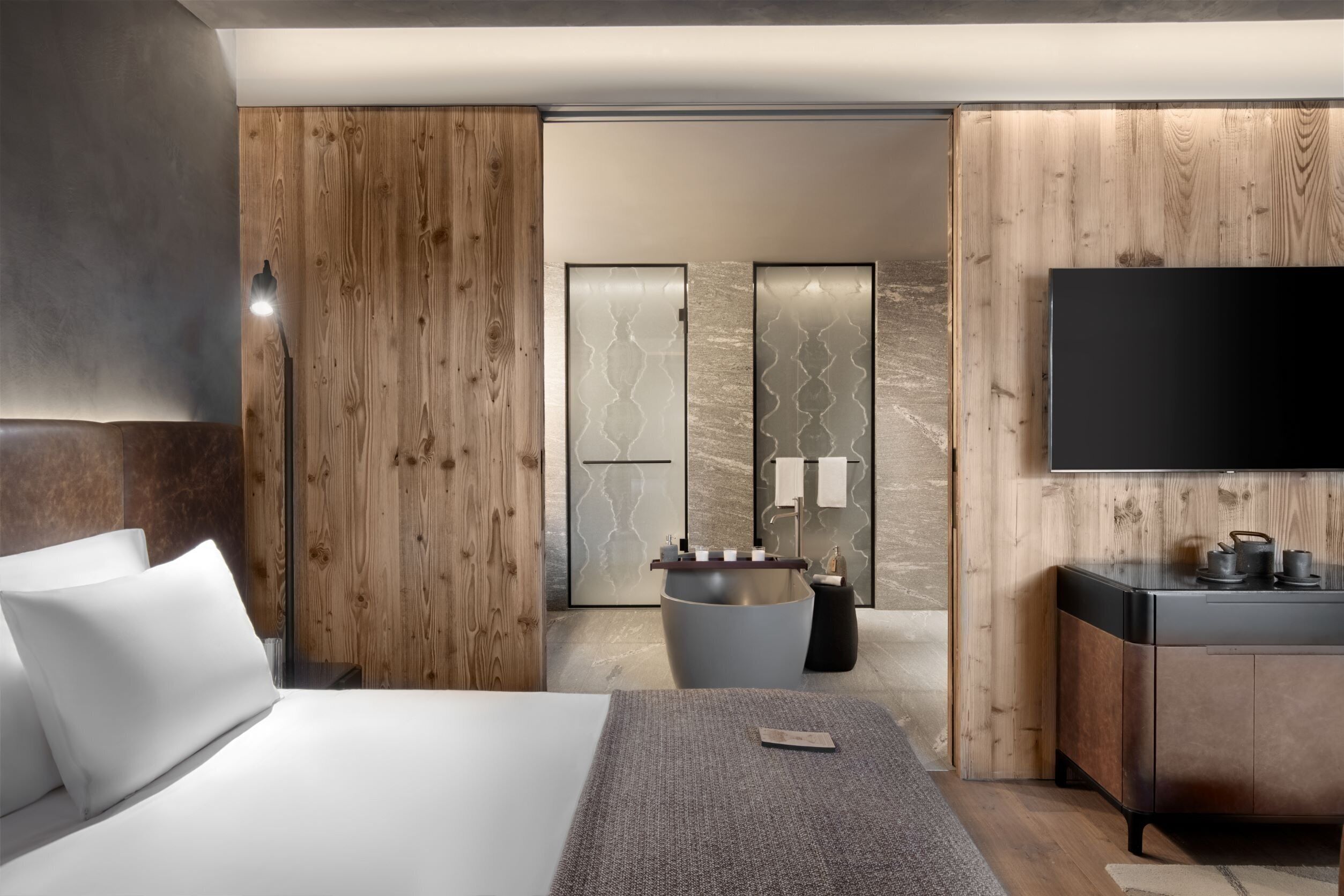 A modern hotel room with a large bed, a flat-screen TV, a built-in sink, and a wooden accent wall.