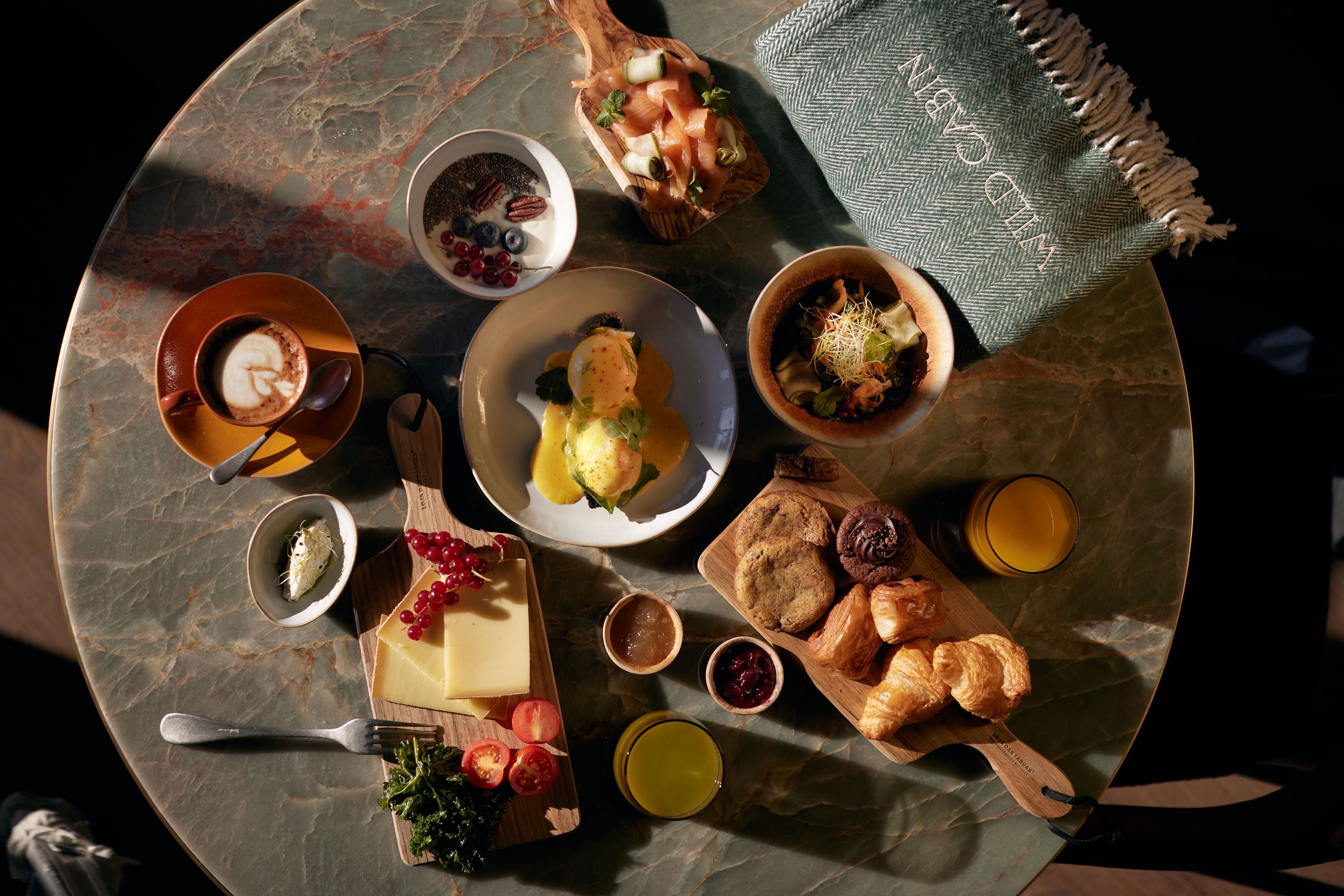 A round table with a variety of food items including cheese, bread, and pastries, along with a cup of coffee and a glass of juice.