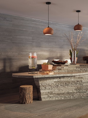 Una zona de bar moderna con encimera de piedra, dos lámparas colgantes, un dispensador de agua de vidrio y plantas decorativas.