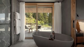 A modern bathroom with a freestanding bathtub, large windows, and a view of a patio area. - Six Senses Crans-Montana (Lens)