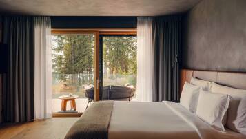 A bedroom with a large bed, a view of the outdoors, and a balcony with a chair and table.