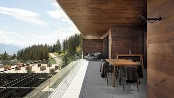 Un balcon avec une table et des chaises en bois, un canapé et une vue sur une forêt et des montagnes.