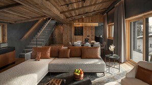 A modern living room with a wooden ceiling, a grey sofa with brown cushions, a coffee table with fruit, and a staircase leading to an upper level. - Six Senses Crans-Montana (Lens)
