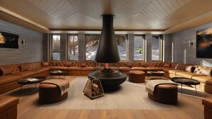 A modern lounge with leather sofas, a central fireplace, and large windows offering a view of the outdoors. - Six Senses Crans-Montana (Lens)