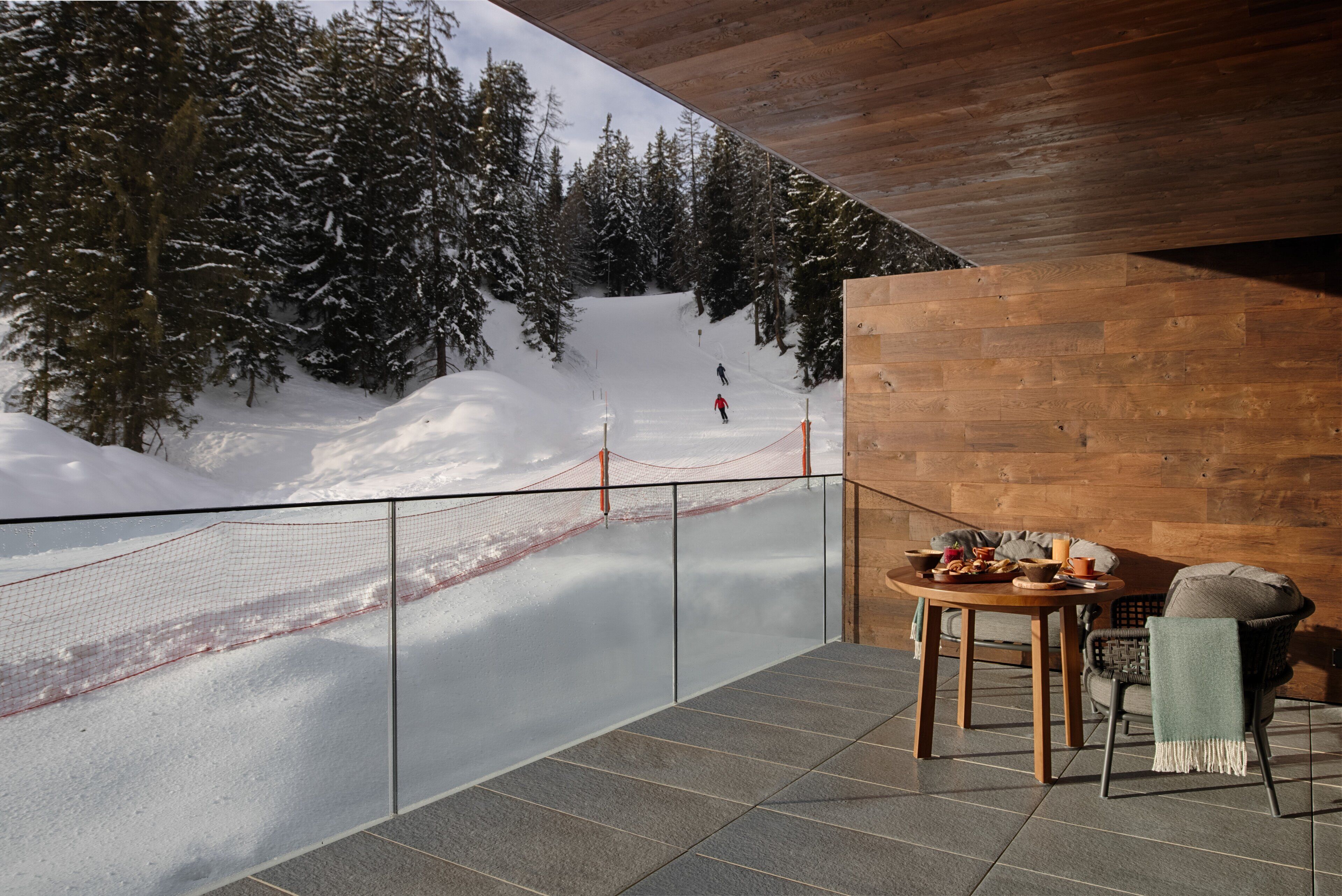 Un balcon donnant sur une pente enneigée, avec une table et des chaises.