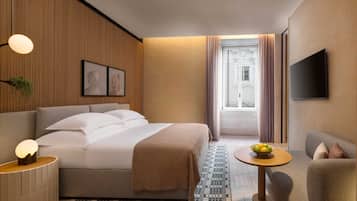 A hotel room with a bed, bedside table, lamp, TV, and a view of the street.