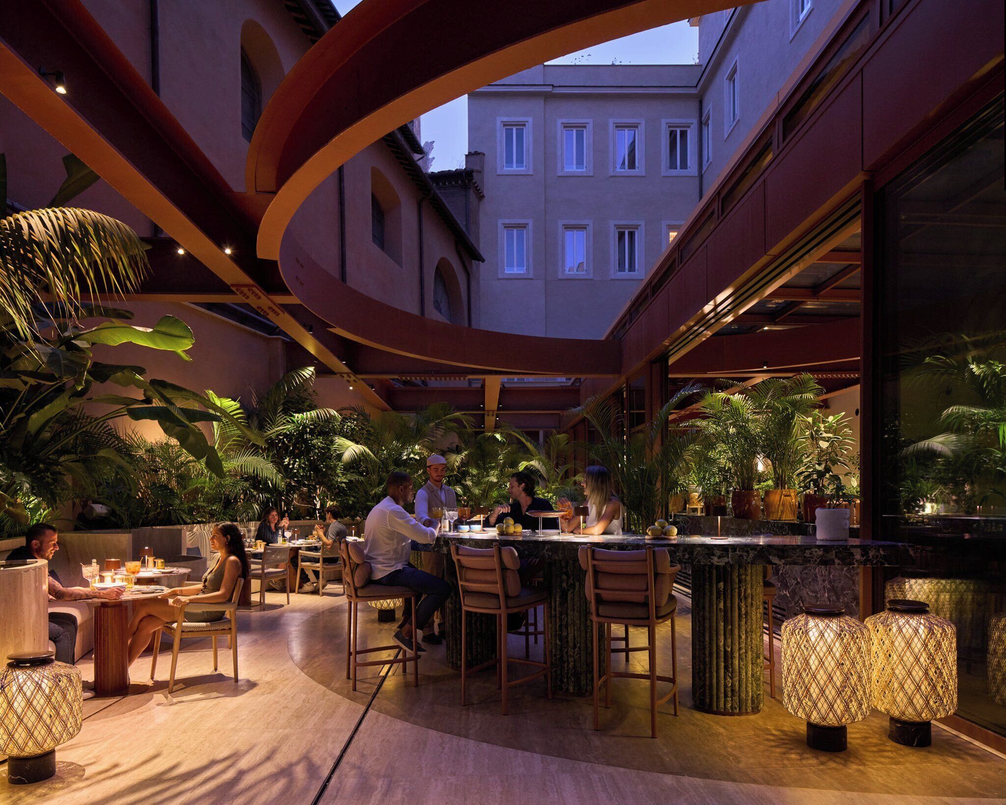 An outdoor dining area with tables and chairs, surrounded by potted plants and a bar area.