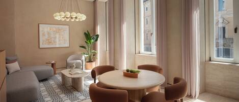 A modern living room with a round table, brown chairs, a sofa, a coffee table, a potted plant, and a hanging light fixture.