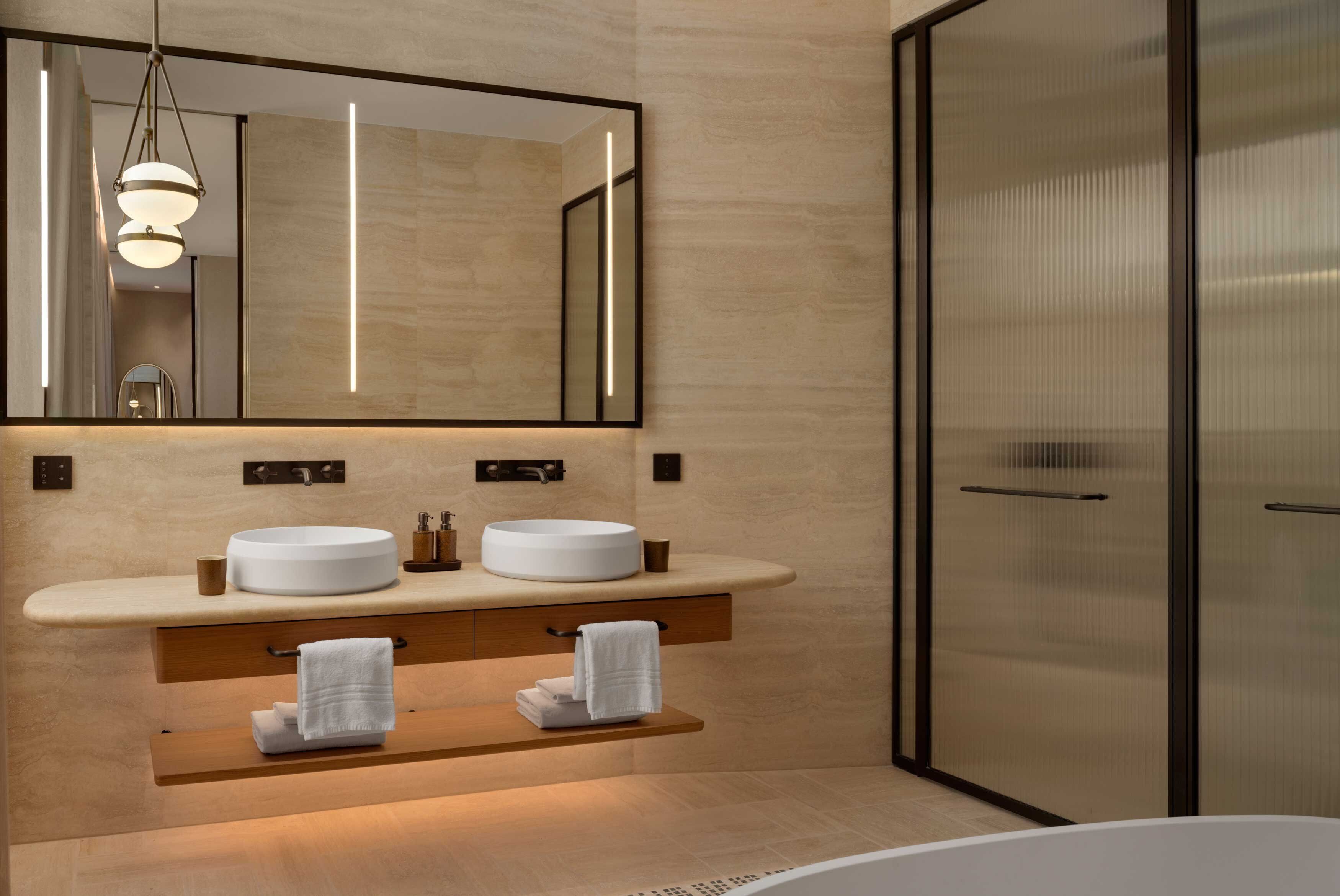 A modern bathroom with a double sink vanity, a large mirror, and a glass shower enclosure.