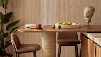 A wooden dining table with two chairs, a potted plant, a bust sculpture, and a bowl of fruit.