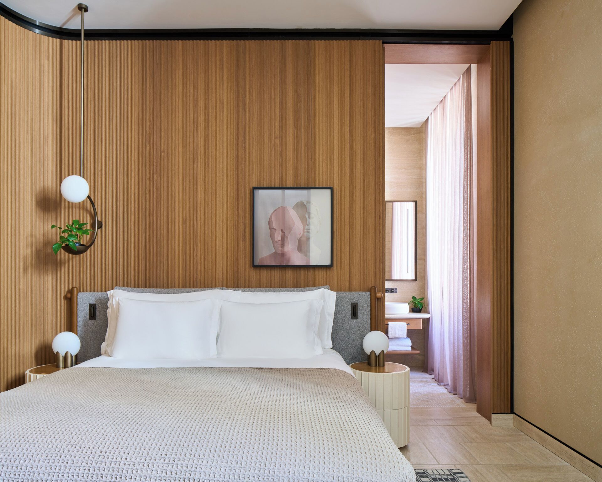 A modern hotel room with a large bed, wooden panel walls, a framed artwork, and a small plant.