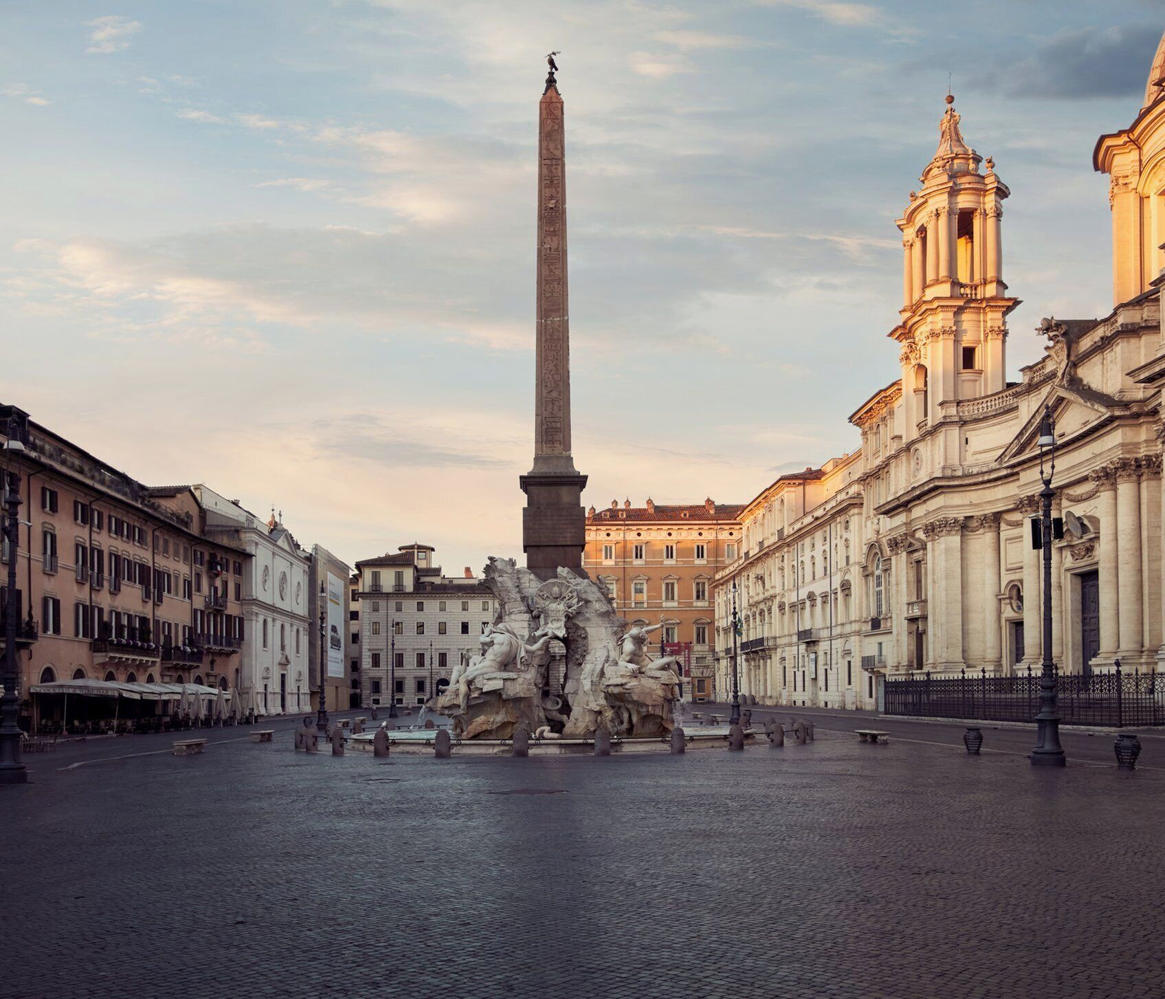 Una piazza storica con un obelisco al centro, una fontana e architettura neoclassica.