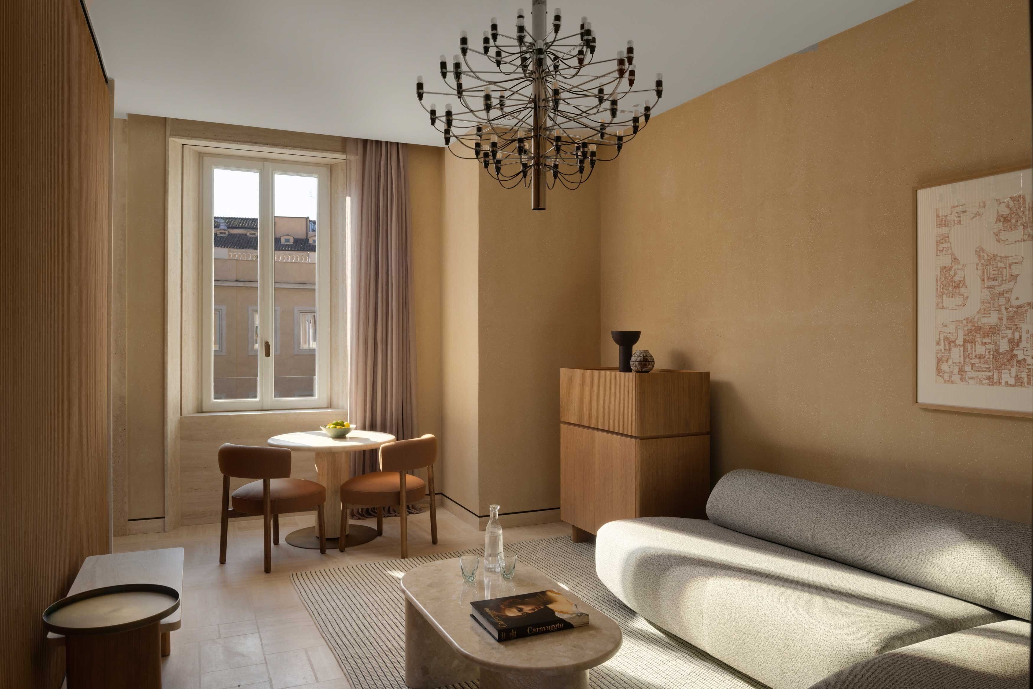 Un salon moderne avec un canapé, une table à manger et des chaises, un lustre, et une vue sur l’extérieur par une fenêtre.