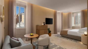 A modern hotel room with a sofa, a small round table with a bowl of fruit, a potted plant, a bed with a bedside table and lamp, and a TV mounted on the wall.