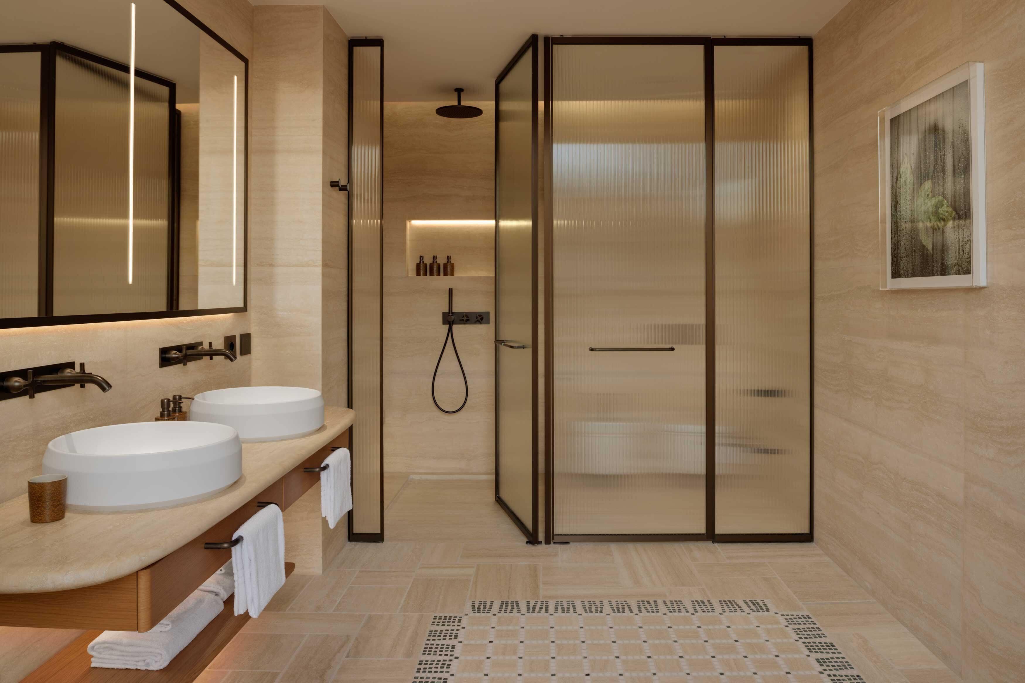 A modern bathroom with two sinks, a glass shower enclosure, and a large mirror.