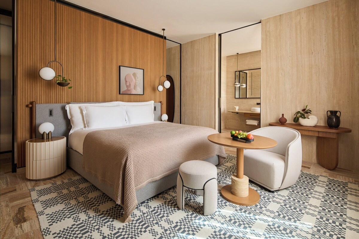 Una camera da letto moderna con un letto grande, comodini, un tavolino con frutta, una sedia e uno specchio.