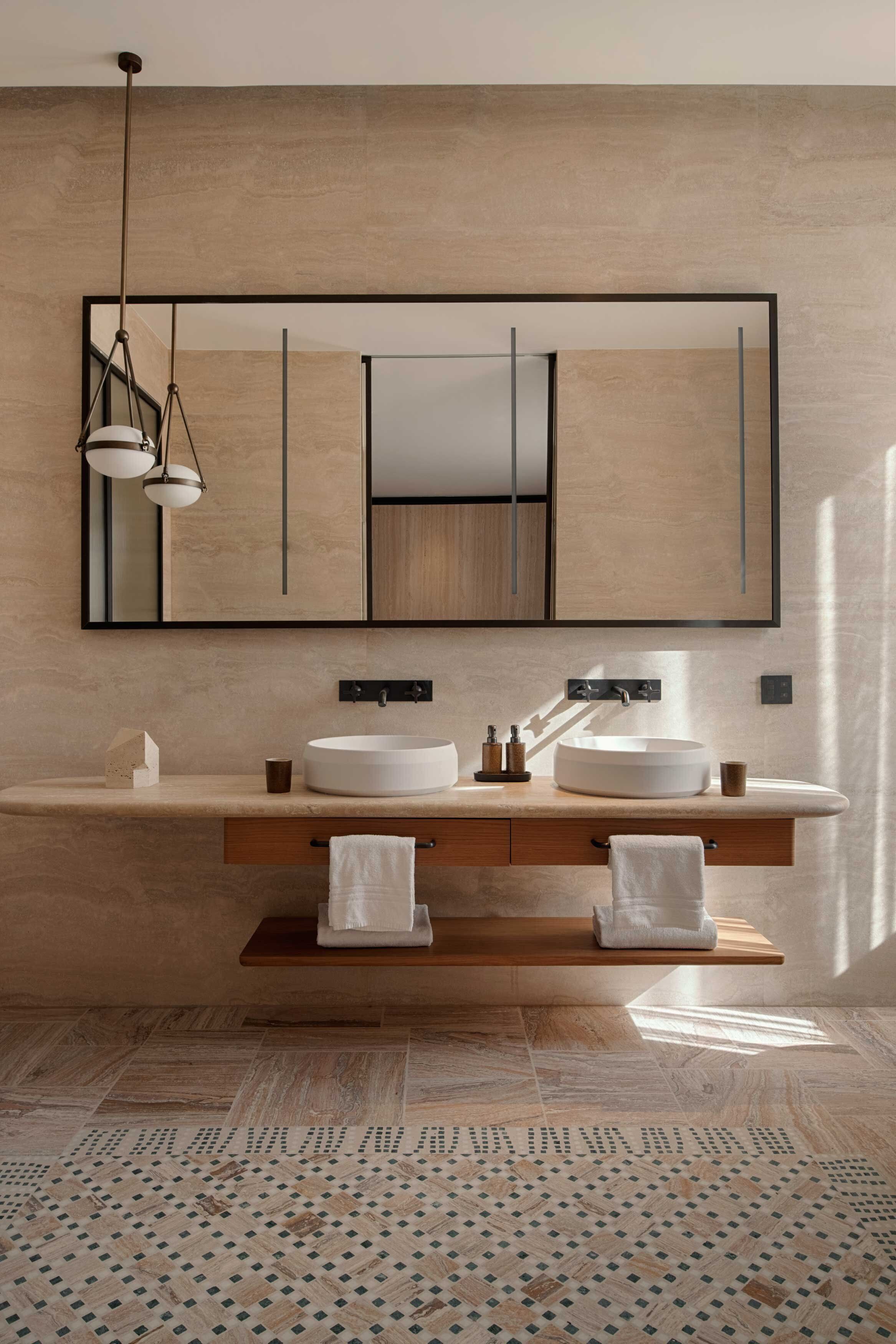 A modern bathroom with two sinks, a large mirror, and a hanging light fixture.