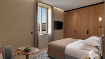Une chambre d’hôtel moderne, avec un lit, une petite table ronde sur laquelle se trouve un saladier de fruits, un canapé et une fenêtre avec des rideaux.