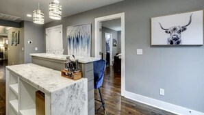 A modern kitchen with a marble countertop, pendant lights, and a blue chair.