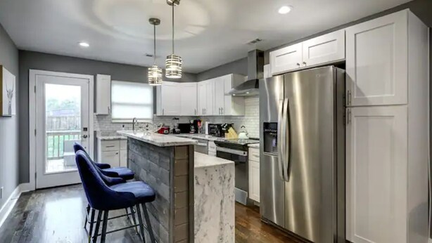 A modern kitchen with white cabinets, a stainless steel refrigerator, and a marble island.