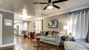 A spacious living room with hardwood flooring, a grey sofa set, a coffee table, and a ceiling fan.
