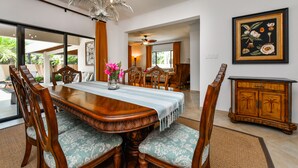 Un coin repas avec une table en bois, des chaises rembourrées, un lustre et une estampe botanique encadrée au mur.