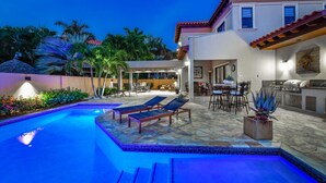 Une piscine avec des chaises longues, un espace patio comprenant une table et des chaises, et un coin cuisine équipé d’une cuisinière et d’un évier.