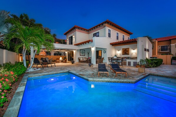A two-story house with a swimming pool, outdoor seating, and a patio area.