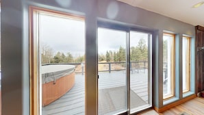 A room with large sliding glass doors leading to an outdoor deck with a hot tub and a view of a forested area.