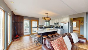A modern kitchen with a central island, bar stools, and a leather sofa in a spacious living area with large windows.