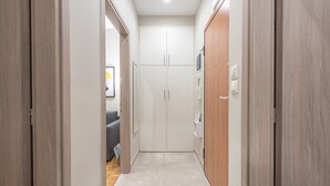 A narrow hallway with a wooden door on the left, a white wardrobe with two doors on the right, and a grey sofa in the background. - Elegant Mavili Suite by Cloudkeys (Athens)